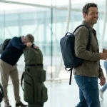 Călător relaxat în aeroport cu doar un rucsac mic, contrastând cu alți pasageri care se chinuie cu genți mari de golf