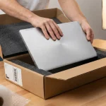 Pregătirea profesională a unui laptop pentru expediere prin curier, cu materiale de protecție și cutie dedicată